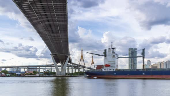 Large suspension bridge over Chao Phraya river with cargo ship - time lapse