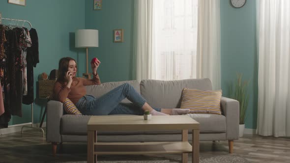Young Girl with Red Apple Lies on Sofa and Talks on Phone