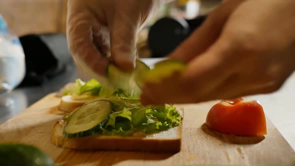 Man's Hands Put Cucumber Slices on a Sandwich