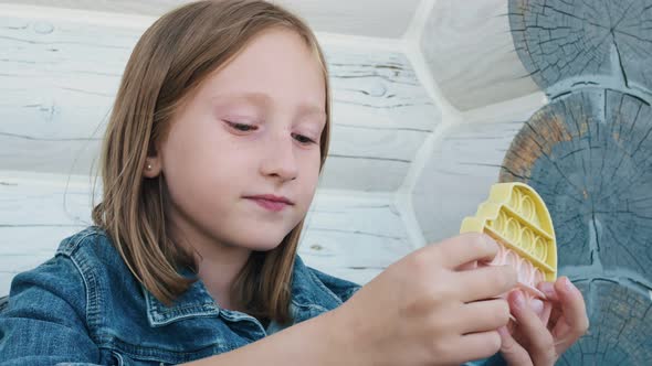 The Blonde Girl is Using the Fashionable Antistress Toy Poppit Trendy for Children and Youth alt