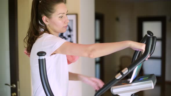 The girl finishes cardio workout, picks up the tablet and walks away. alt