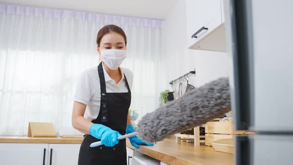Asian cleaning service woman worker wear face mask, cleaning in kitchen room at home. alt