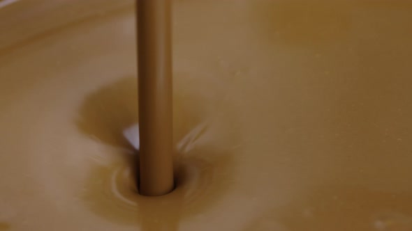 Jet of Molten Chocolate Pours Into Container Forming Funnel on Glossy Surface