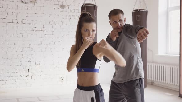 An Experienced Trainer Puts the Technique of Blows To a Young Girl in the Boxing Hall