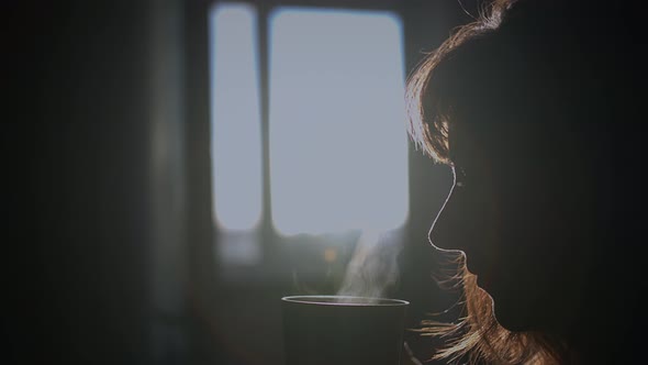 Silhouette of a Pretty Woman Drinking Coffee Early in the Morning Sun Rays