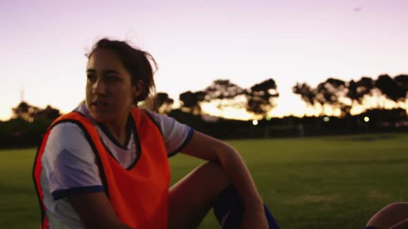 Female soccer team sitting on the ground while talking on soccer field. 4k alt