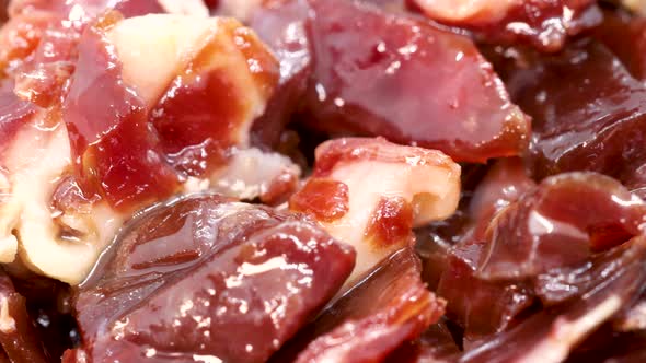 Spanish jamón ibérico small pieces, close up view in 4k. Serrano ham rotating, macro shot. alt