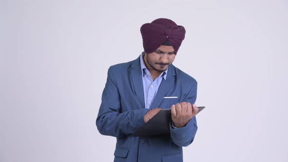 Stressed Indian Sikh Businessman Showing Clipboard and Giving Thumbs Down alt