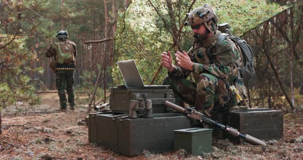A Bearded Commander in a Military Uniform in a Tactical Vest with a Helmet on His Head Chatting alt