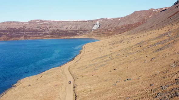 Car On Dirt Track By Fjord Towards Waterfall On Mountain alt