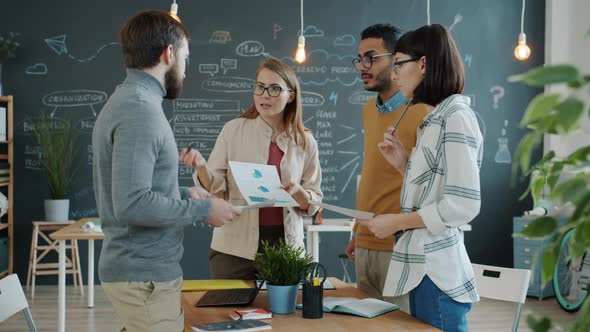 Creative Team Discussing Project Looking Through Charts and Graphs in Office alt