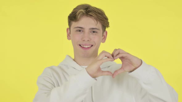 Young Man Showing Heart Shape By Hands on Yellow Background alt