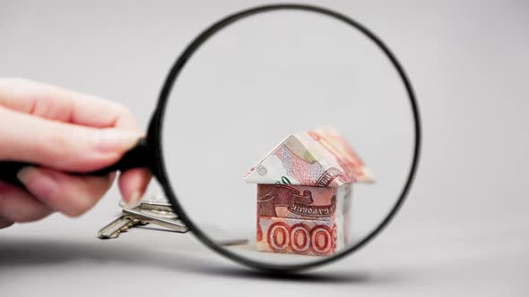 Hand shows zoomed with magnifier glass key with keychain and paper origami of house alt