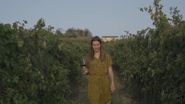 Beautiful Young Woman Walks Through The Vineyards With Glass Of Wine