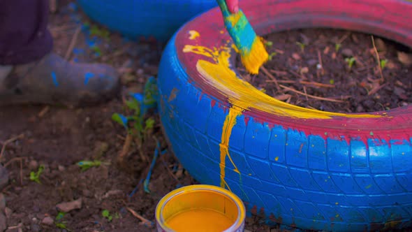 Close Up of Unrecognizable Person Paints Wheel with Yellow Paint on Street alt