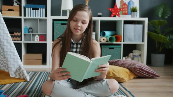 Happy Child Reading Book Turning Pages and Smiling Sitting on Floor at Home alt