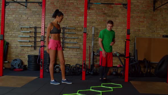 Fitness Instructor Showing Agility Ladder in and Out Drills to Female Athlete alt