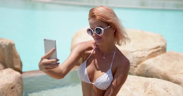 Smiling Woman in Swimwear Taking Selfie on Smartphone Showing Two Fingers alt