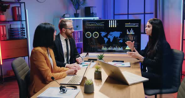 Businesspeople Sitting at Meeting Table in Evening Office and Making Unity and Trust Symbol alt