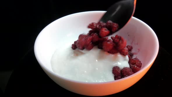 A white bowl of raspberries in cream rotates against a dark background. alt