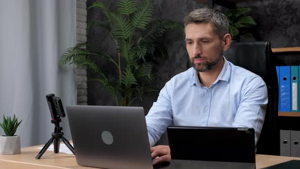 Adult Businessman Works for Laptop Online Chatting Turns to Camera and Smiles alt