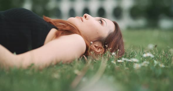 A young woman lying on the grass looking at the sky and moving her head alt