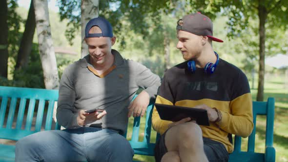Gay Couple with Gadgets Enjoying Leisure in Park alt