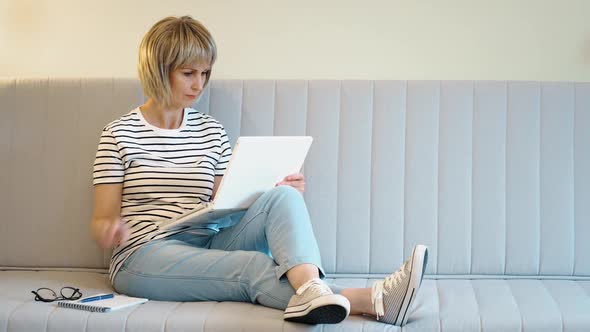 An Elderly Beautiful Woman Works at Home at a Laptop in the Home Office