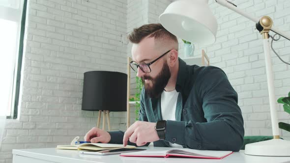 Bearded Man Learn Online Courses Using a Tablet and Write Notice in His Notebook alt