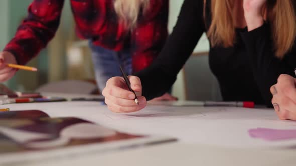 Closeup View of Hands of Young Creative People Drawing a Draft with Colored Pencils on White Sheets alt
