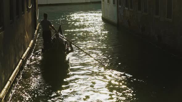 Silhouette of Gondolier Steering Boat in Venice Street, Sun Reflection in Water alt