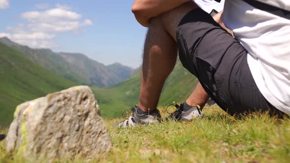 A Man Sits on the Grass at the Top of the Mountain Looks at the Mountain Range