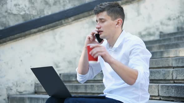 Businessman Sitting On Stairs And Talking With Colleague On Mobile Phone. alt