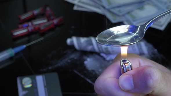 Addict with lighter is cooking heroin on spoon. Male drug user is preparing drugs for using alt