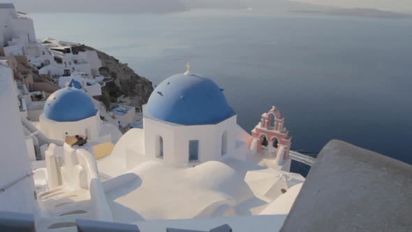 Picturesque view of blue church domes and a pink church bell in Oia, Santorini. alt