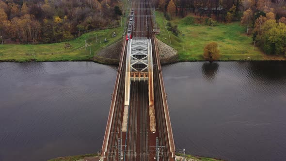 Red Passenger Train Passes Over the Bridge Over the River in Golden Autumn, Aerial View alt