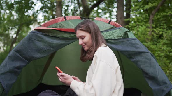 A Beautiful Young Woman Uses Phone in a Camp While Sitting in a Tent