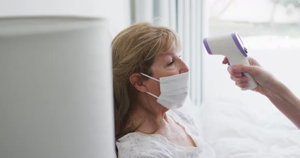 Senior woman wearing face mask getting her temperature measured at home alt
