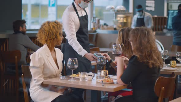 Happy Friends Using Phone Making Contactless Payment in Restaurant Before Leaving alt