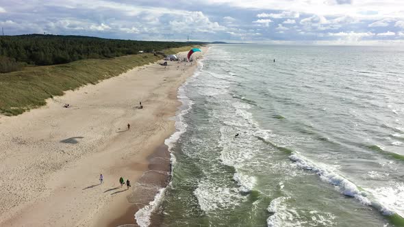 AERIAL: Flying Over Sandy Beach with People Walking and Surfer Trying to Surf with Wind Kite