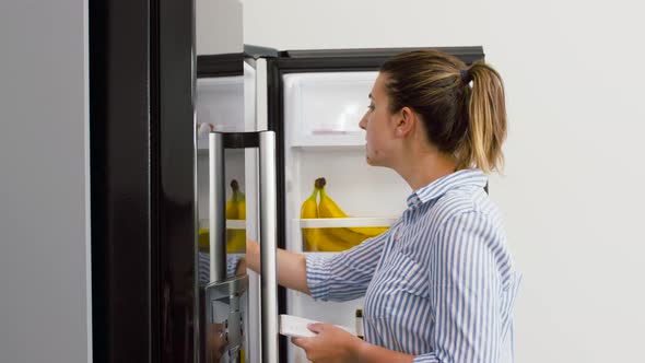Woman Making List of Necessary Food at Home Fridge alt