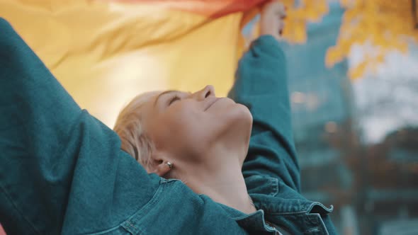 Beutiful Young Woman with Short Hair Lifing Rainbow Flag From Her Head in the Air alt