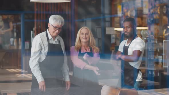 View Through Window of Happy Diverse Waiters Looking at Camera with Hands Crossed in Restaurant alt
