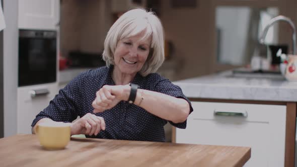 Senior Adult using smart watch at home on kitchen table