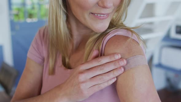 Happy caucasian mature woman showing plaster on arm where she was vaccinated against coronavirus alt