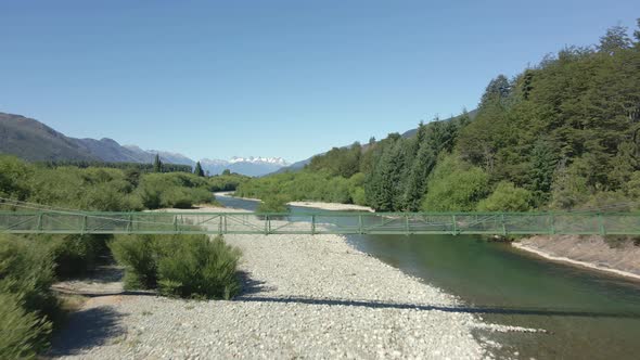 Aerial dolly in of river and elevated bridge surrounded by pine trees and mountains, Pasarela Rio Az alt