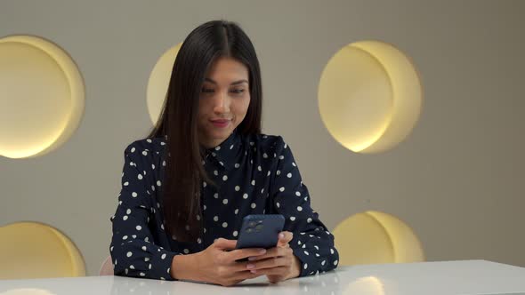 An Asian Woman Sits at Her Desk in the Office Holds a Smartphone Receives a Message From the Bank alt
