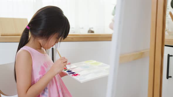 Asian young happy kid girl coloring on painting board in living room. alt