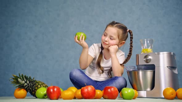 Pretty little girl sitting on the desk and eating apple.  alt