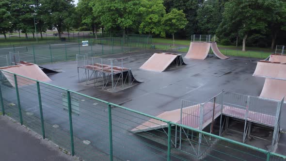 Aerial view flying low over fenced skate park ramp in empty closed playground alt